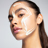 A photo of a model with a slicked back ponytail looks into the camera with artistically placed Daydream Cream Adaptogen Moisturizer swipes on her face. The buttery yellow color contrasts with her tan 
