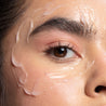 A closeup photo of the No Baggage Adaptogen Eye Cream applied artistically to the models face around the eye area. Emphasizing the thick product texture and light pink color of the formula.