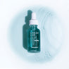 A photo of Alpha-Bet Elixir Super Power Facial Oil placed lying face up on a pool of the products light turquoise content