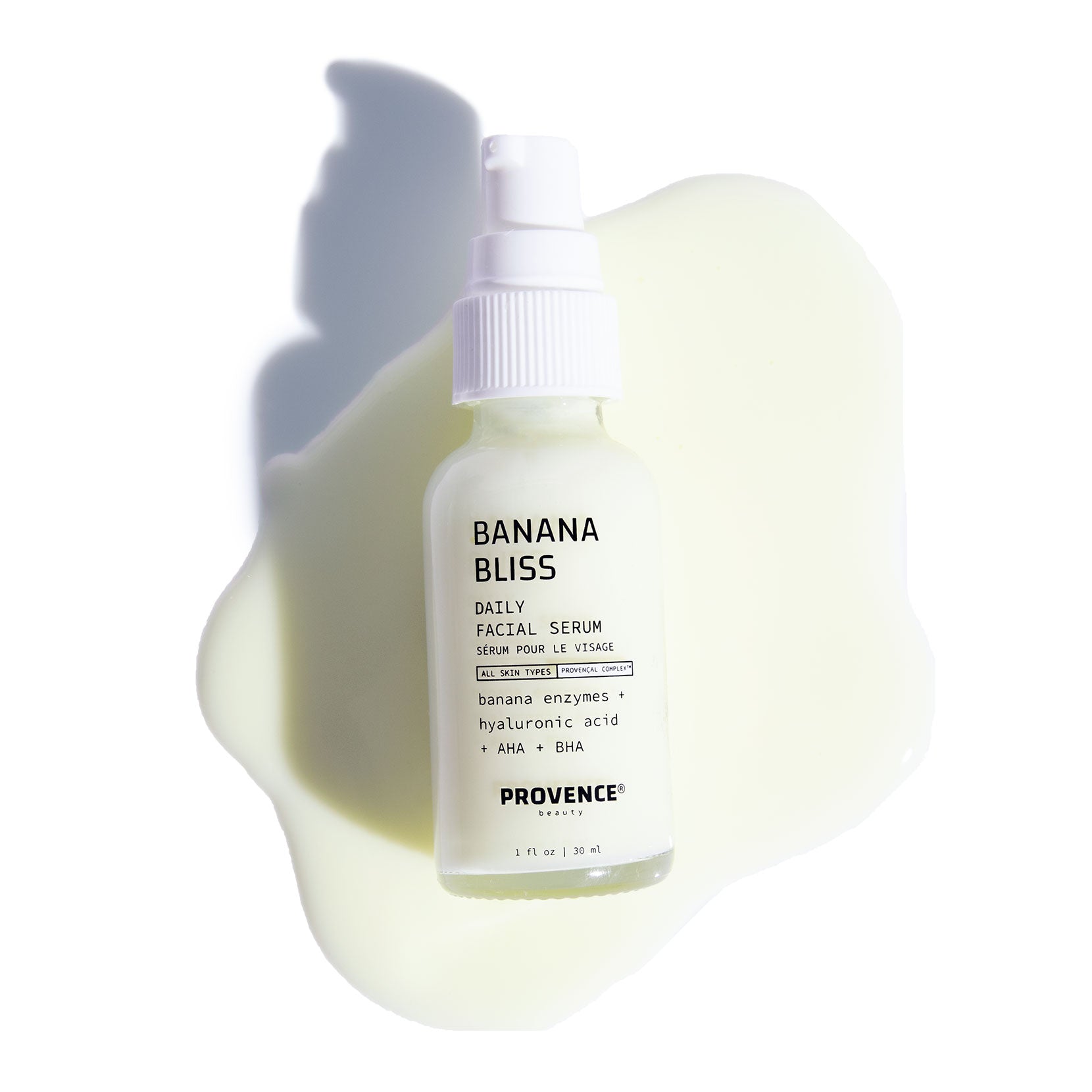 A photo of Banana Bliss Daily Facial Serum laying face up on the products content against a white background. The serum product is spreading thinly from the center away from the bottle.