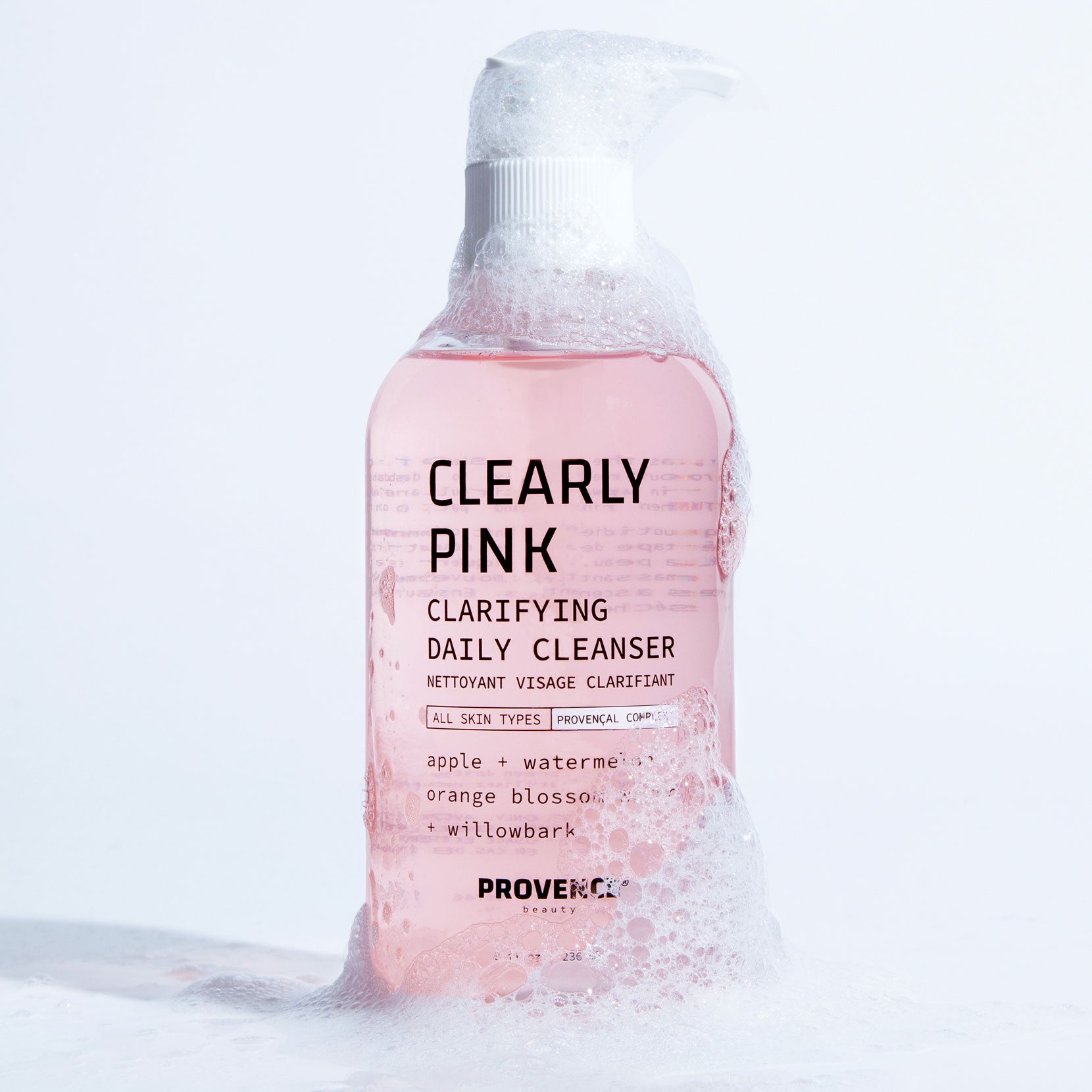 A photo of the Clearly Pink Clarifying Cleanser against a white background with foaming bubbles around the bottom and top of the glass bottle. Showcasing the products lively and enriched content.